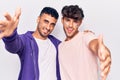 Young gay couple drawing rainbow lgtbq flag on face looking at the camera smiling with open arms for hug