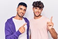 Young gay couple drawing rainbow lgtbq flag on face smiling and looking at the camera pointing with two hands and fingers to the