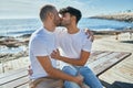 Young gay couple kissing sitting on the bench at the beach promenade Royalty Free Stock Photo