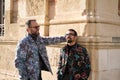 Young gay couple look at each other happily leaning against the wall of a historic building in Seville, Spain. The couple are