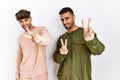 Young gay couple standing over isolated white background smiling looking to the camera showing fingers doing victory sign Royalty Free Stock Photo