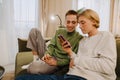 Young gay couple talking and using mobile phone while resting on couch Royalty Free Stock Photo