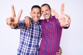 Young gay couple of two men wearing casual clothes smiling with tongue out showing fingers of both hands doing victory sign Royalty Free Stock Photo