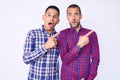 Young gay couple of two men wearing casual clothes surprised pointing with finger to the side, open mouth amazed expression Royalty Free Stock Photo