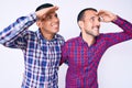 Young gay couple of two men wearing casual clothes very happy and smiling looking far away with hand over head Royalty Free Stock Photo