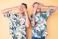 Young gay couple of two men wearing summer hat and hawaiian shirt covering eyes with hands smiling cheerful and funny Royalty Free Stock Photo