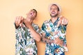 Young gay couple of two men wearing summer hat and hawaiian shirt laughing at you, pointing finger to the camera with hand over Royalty Free Stock Photo