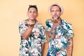 Young gay couple of two men wearing summer hat and hawaiian shirt looking at the camera blowing a kiss with hand on air being Royalty Free Stock Photo