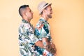 Young gay couple of two men wearing summer hat and hawaiian shirt looking to side, relax profile pose with natural face and Royalty Free Stock Photo