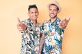 Young gay couple of two men wearing summer hat and hawaiian shirt smiling cheerful offering palm hand giving assistance and Royalty Free Stock Photo