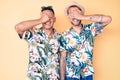 Young gay couple of two men wearing summer hat and hawaiian shirt smiling and laughing with hand on face covering eyes for Royalty Free Stock Photo