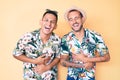 Young gay couple of two men wearing summer hat and hawaiian shirt smiling and laughing hard out loud because funny crazy joke with Royalty Free Stock Photo