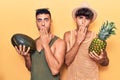 Young gay couple wearing summer clothes holding melon and pineapple covering mouth with hand, shocked and afraid for mistake Royalty Free Stock Photo