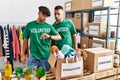 Young gay couple wearing volunteer t shirt at donations stand checking the time on wrist watch, relaxed and confident