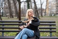 Young generation Z hipster girl sitting in park on a bench with her adopted dog, whom she rescued from the street from starvation Royalty Free Stock Photo