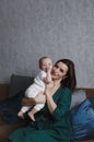 A young gentle happy mother hugs her newborn baby, smiling, sitting at home on the couch. Royalty Free Stock Photo