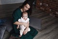 A young gentle happy mother hugs her newborn baby, smiling, sitting at home on the couch. Royalty Free Stock Photo