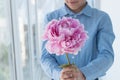 Young gentlemen in blue shirt hold huge gentle pink peony in hands and smile.