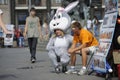 Young girl, an advertising promoter in animal costume of hare, having break near man street vendor