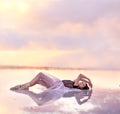 A young girl in an airy dress lies in the water of a pink lake.