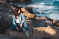 Young girl alone sitting on rocks by the sea in relaxed pose