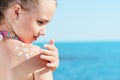 Young girl applyng sun protector cream at her shoulder on the beach close to tropical turquoise sea under blue sky Royalty Free Stock Photo