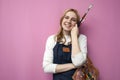 Young girl artist holds brushes and a palette and smiles on a pink background, student of art school, profession of an artist