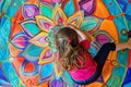 A young girl artist is joyfully creating a vibrant mandala on the floor using paint, showcasing her creativity and love Royalty Free Stock Photo