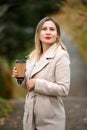 A young girl in the autumn park drinks coffee.