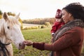 Young Girl On Autumn Walk With Mother Stroking Horse