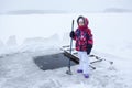 Young girl with axe in hand for ice cutting is standing near ice-hole at lake