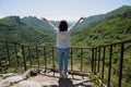 A young girl with a backpack enjoys the beauty of nature, looking at the view with outstretched arms at the top of the mountain