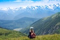 A young girl with a backpack sits on the top of a mountain in Georgia and contemplates the landscape. 