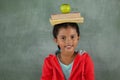 Young girl balancing books and apple on her head