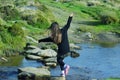 Young girl balancing on stepping stones across a stream .