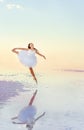 Young girl ballerina makes jumps in the water of a salt lake.