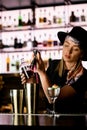 Young girl bartender accurate pours red syrup from jigger into one of steel shaker glasses standing on bar Royalty Free Stock Photo