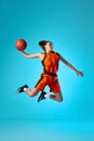 Young girl, basketball player in motion, throwing ball in a jump against blue studio background in neon light. Slam dunk