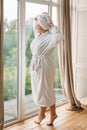 Young girl in a bathrobe and turban in the spa at the big window