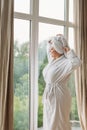 Young girl in a bathrobe and turban in the spa at the big window