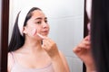 Young girl in bathroom mirror using quartz facial roller to massage her cheek. Skin care at home.