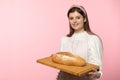 A young attractive saleswoman from a bakery shop holds a loaf of wheat flour bread on a wooden tray. The whole on a Royalty Free Stock Photo