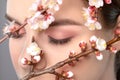 Young girl with beautiful nude make-up, thick eyebrows. Beautiful hazel eyes close up. Near her are beautiful blooming spring Royalty Free Stock Photo