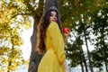 Young girl with beautiful yellow dress and curly hair holding in hand red apple on trees background Royalty Free Stock Photo