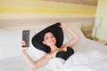 Young girl in a big hat makes selfie on a smartphone while lying in bed.