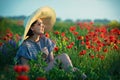 Young girl in a big hat sitting on a poppy field in sunset Royalty Free Stock Photo