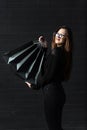 Young girl in black clothes holds shopping bags against black wall. Vertical frame