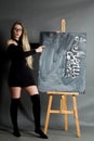 A young girl in a black dress and hetaera, with long hair and glasses, points to a chalkboard Royalty Free Stock Photo