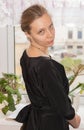 Young girl in black dress is standing at window and is looking over her shoulder at camera. Royalty Free Stock Photo