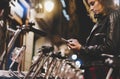 Young girl in black leather jacket using in hands screen smartphone on background bokeh light in night city street, hipster biking Royalty Free Stock Photo